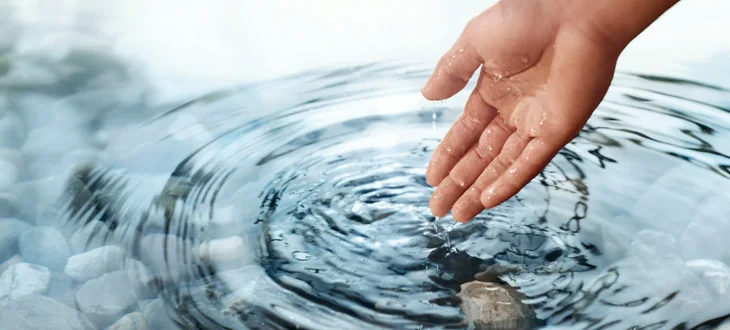 A hand touching the surface of clear water
